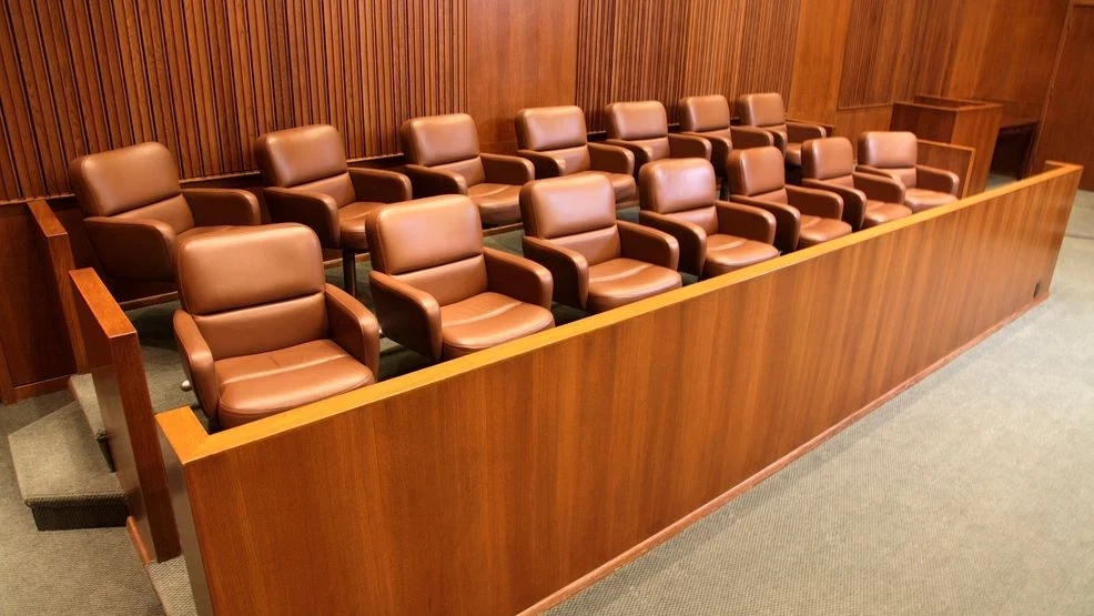 Empty jury box with two rows of brown leather chairs inside a wooden courtroom.